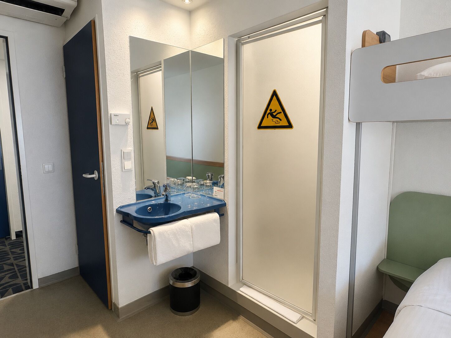 A hotel bathroom with a sink, mirror, towel rack, and a trash bin.