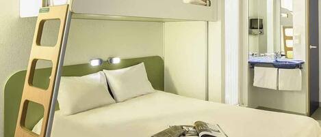 A bunk bed with a ladder, a bedside table, a mirror, and a bathroom with a sink and towel rack.
