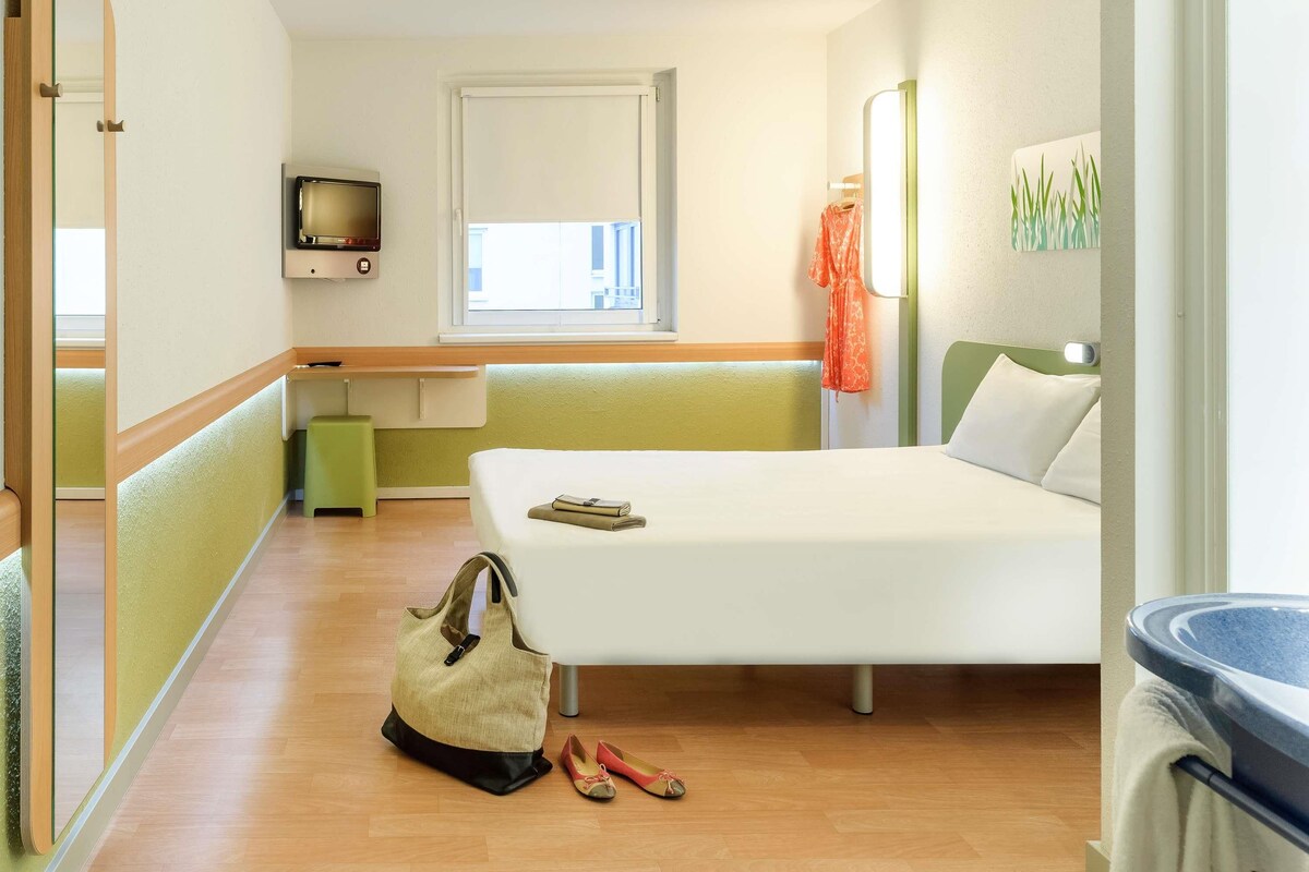 A hotel room with a bed, a TV, a window, a desk, and a bathroom.