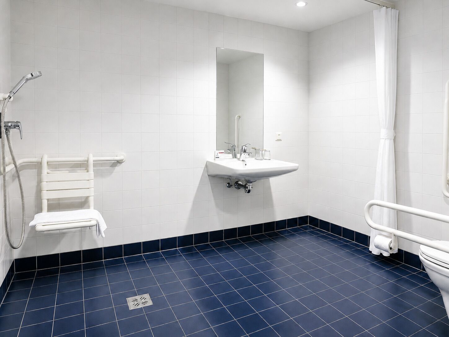 A bathroom with white tiles, a sink, a mirror, a shower, and a toilet.