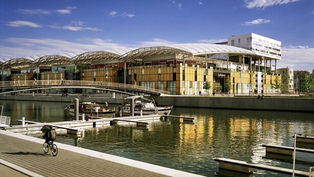 A waterfront area with a modern building, a bridge, and a dock with boats. - ibis budget Lyon Gerland (Lyon)