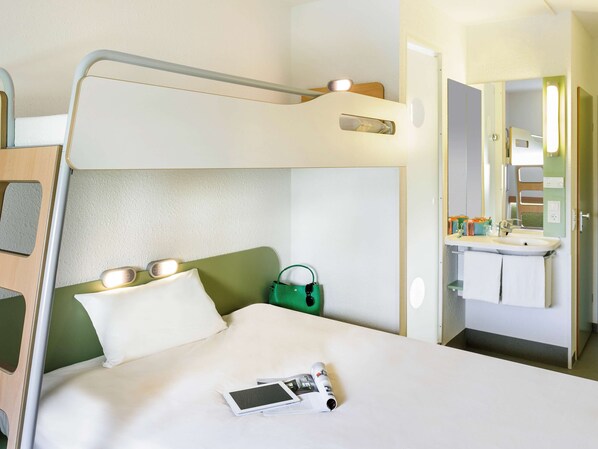 Cozy hotel room with a bunk bed and single bed, featuring a bedside table and bathroom with sink and mirror.