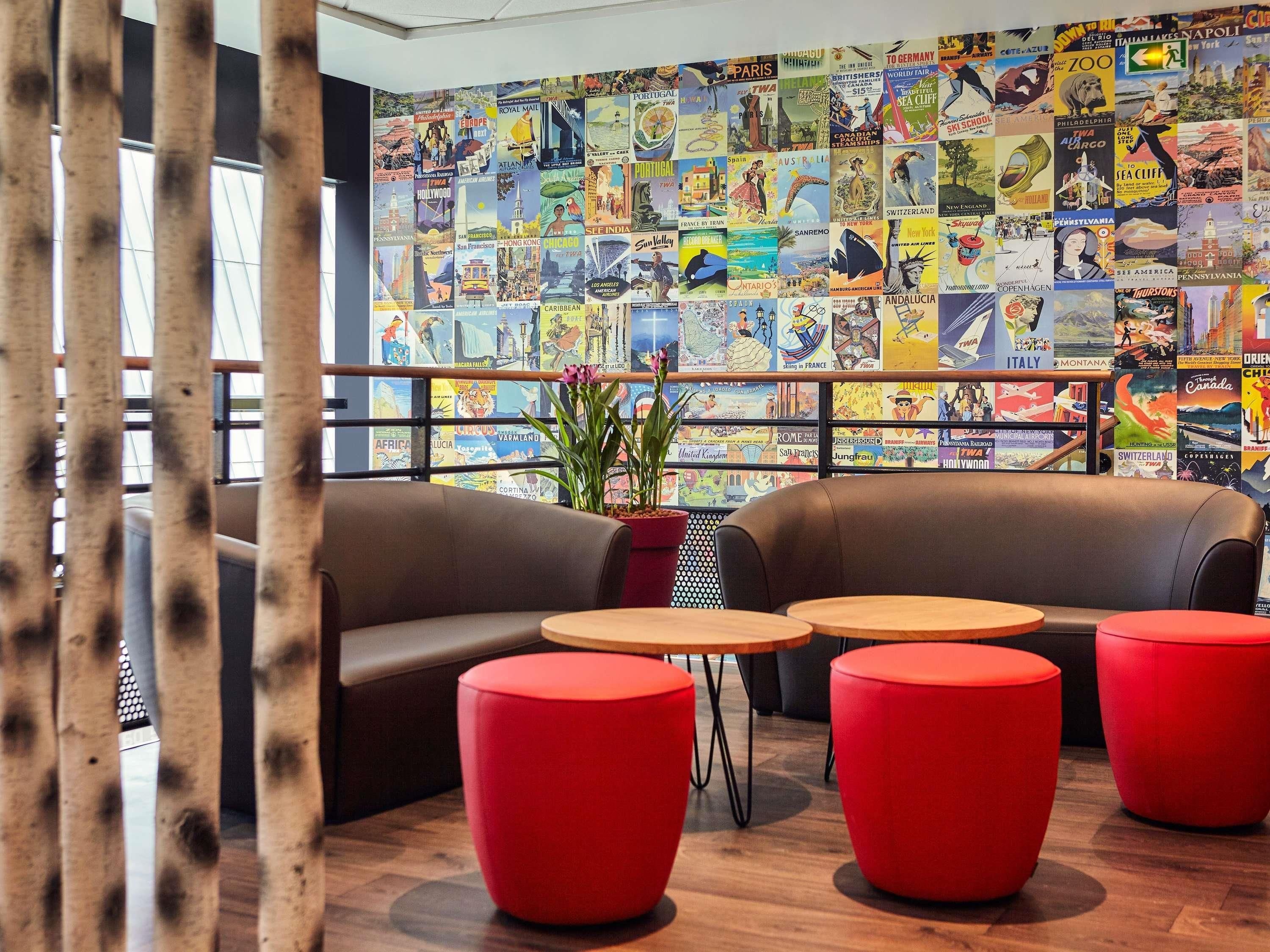 A lounge area with a wall of travel posters, two leather sofas, and red ottomans.