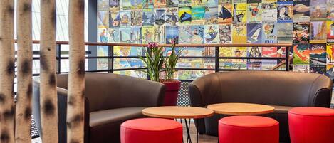 A lounge area with a wall of travel posters, two leather sofas, and red ottomans.