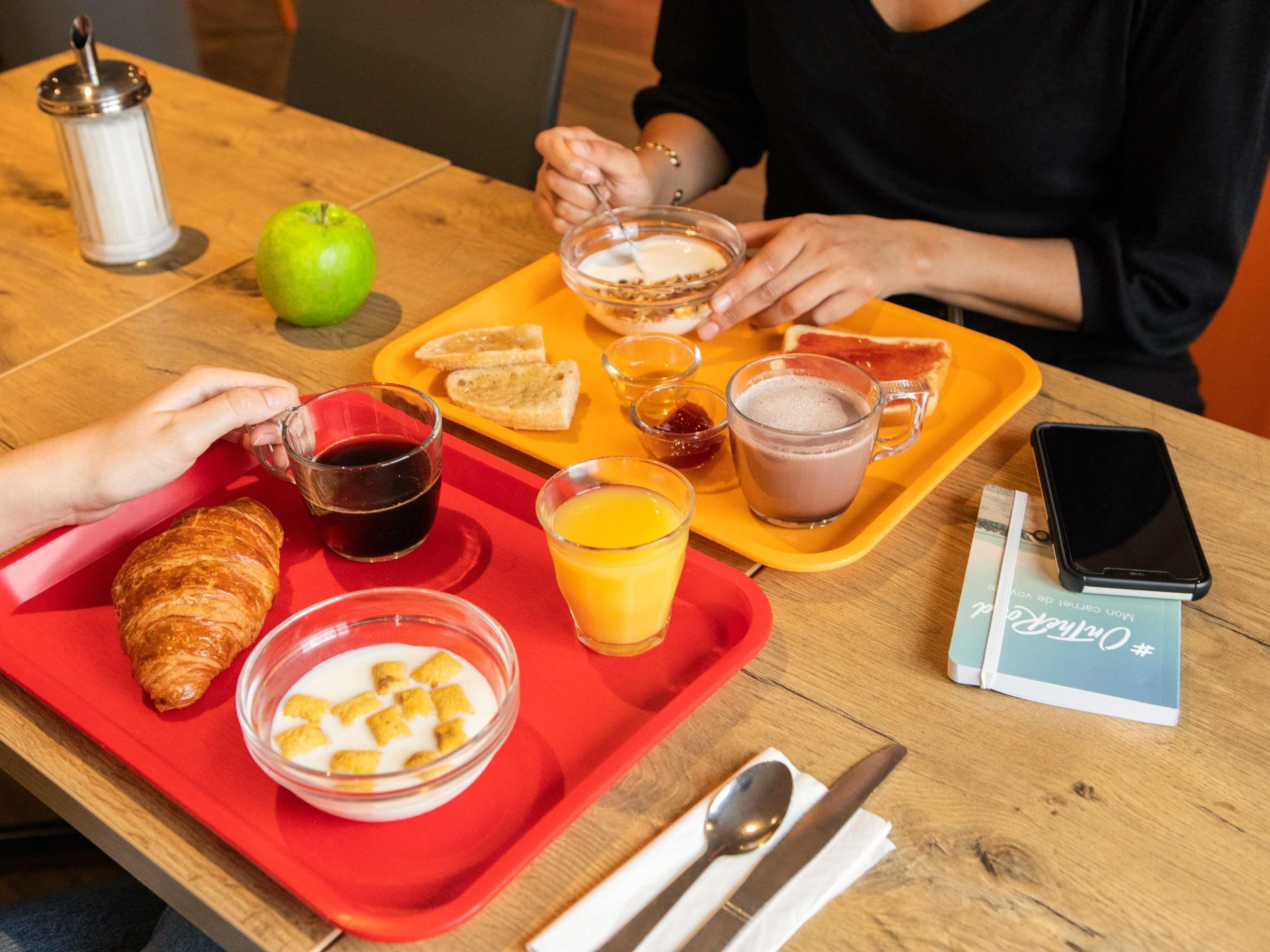 Een ontbijfwagen met croissants, cornflakes, sap en koffie op een houten tafel.