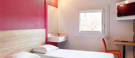 A hotel room with a bed, a window, a desk, and a chair.