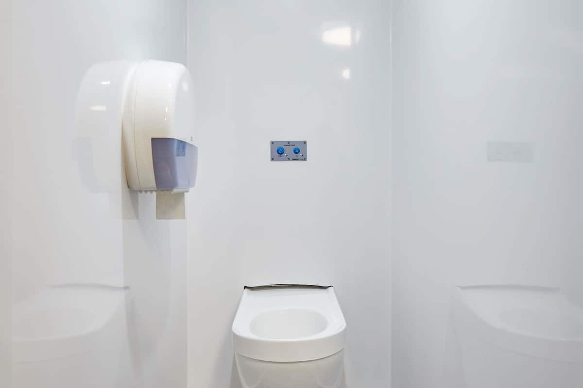 Un baño moderno con inodoro blanco, secador de manos y botón de descarga.