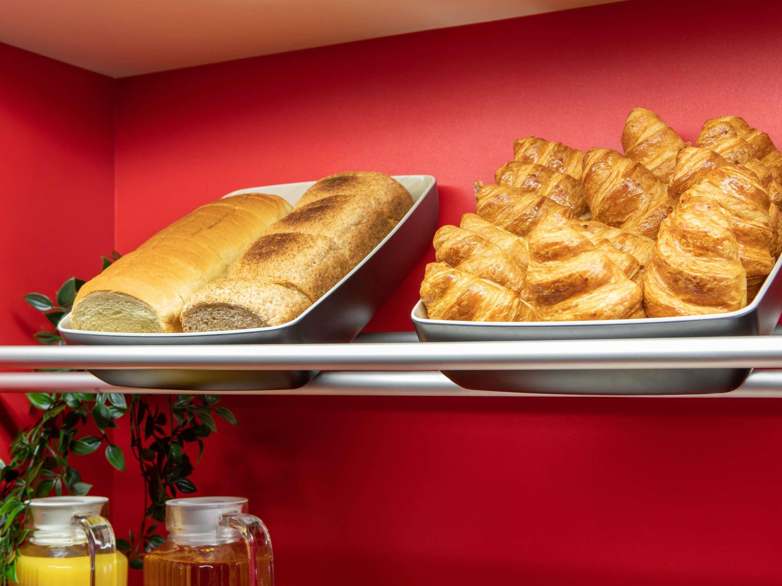 A tray of bread and croissants on a red wall.