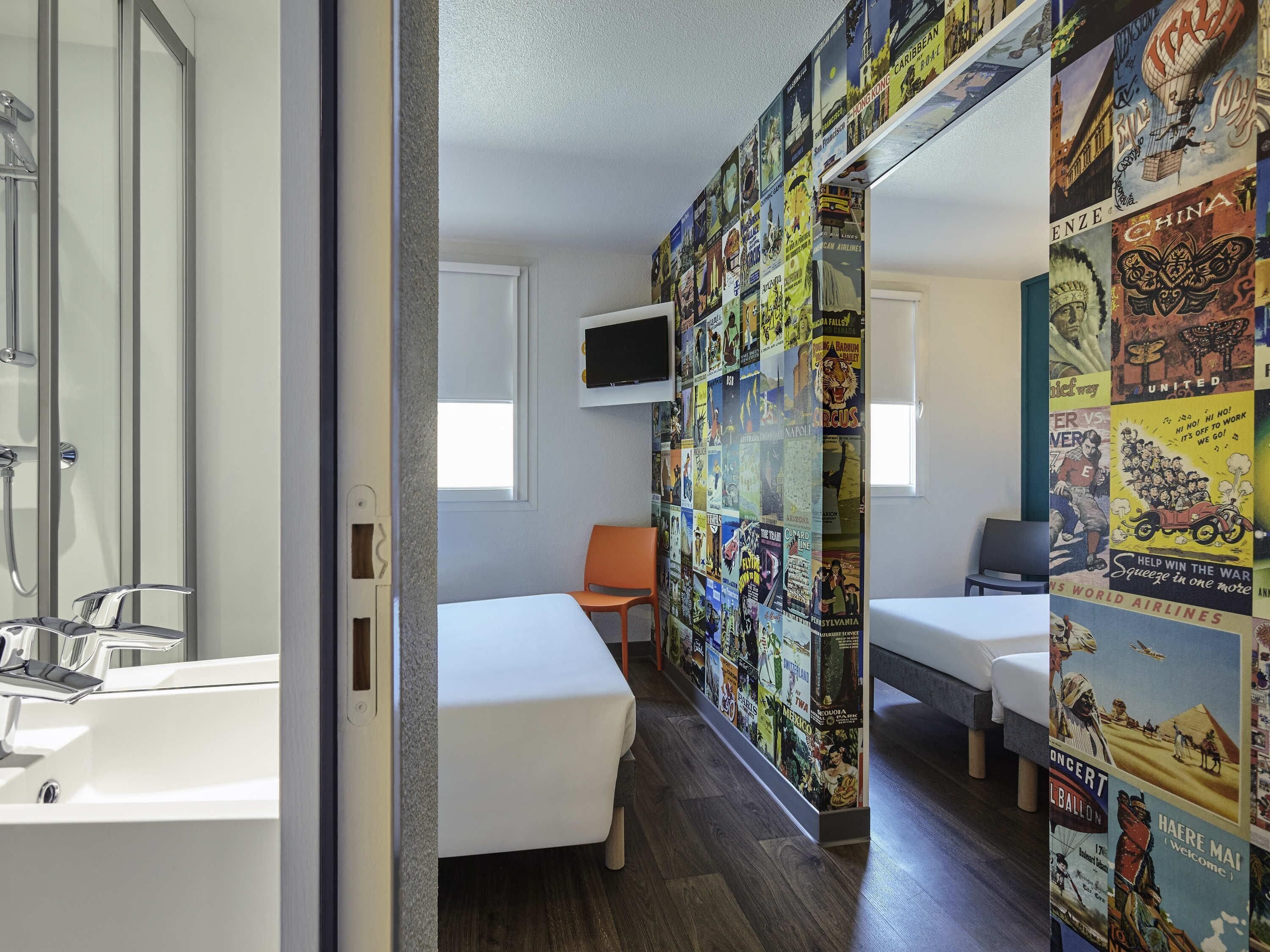 A hotel room with a shower, a bed, a TV, and a wall decorated with vintage travel posters.