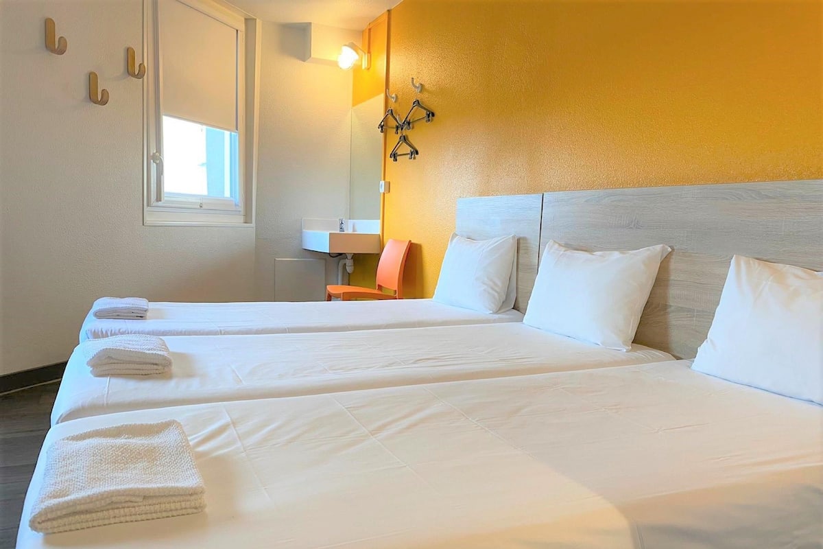 A hotel room with two beds, a window, a sink, and a mirror.