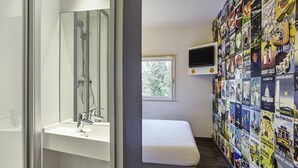 A bathroom with a shower, a sink, a bench, and a wall decorated with travel posters. - hotelF1 Paris Porte de Châtillon (Paris)