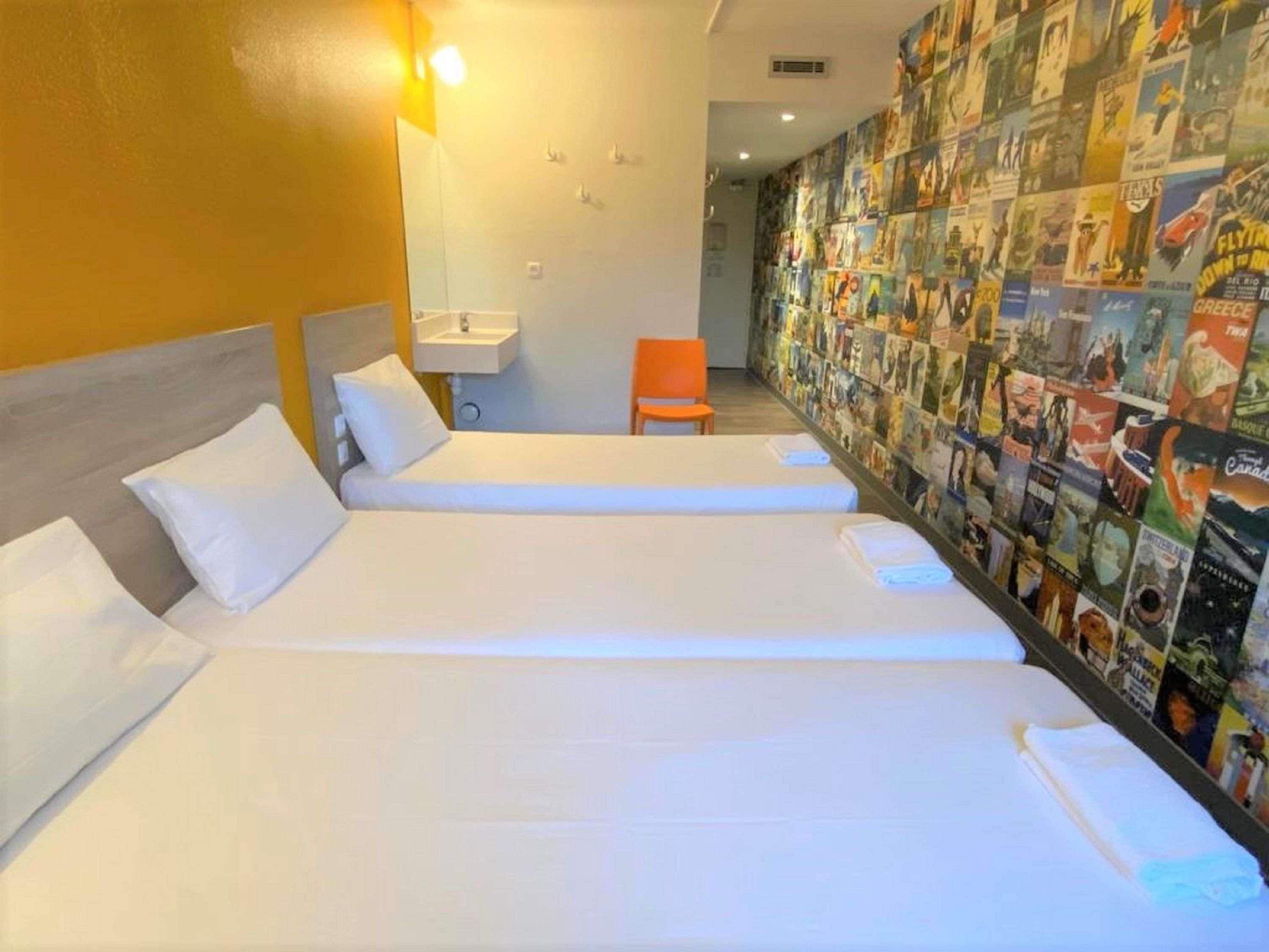 A hotel room with two single beds, a small sink, and a chair.