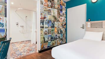 A hotel room with a bed, a shower, a wall decorated with travel posters, and a blue accent wall.