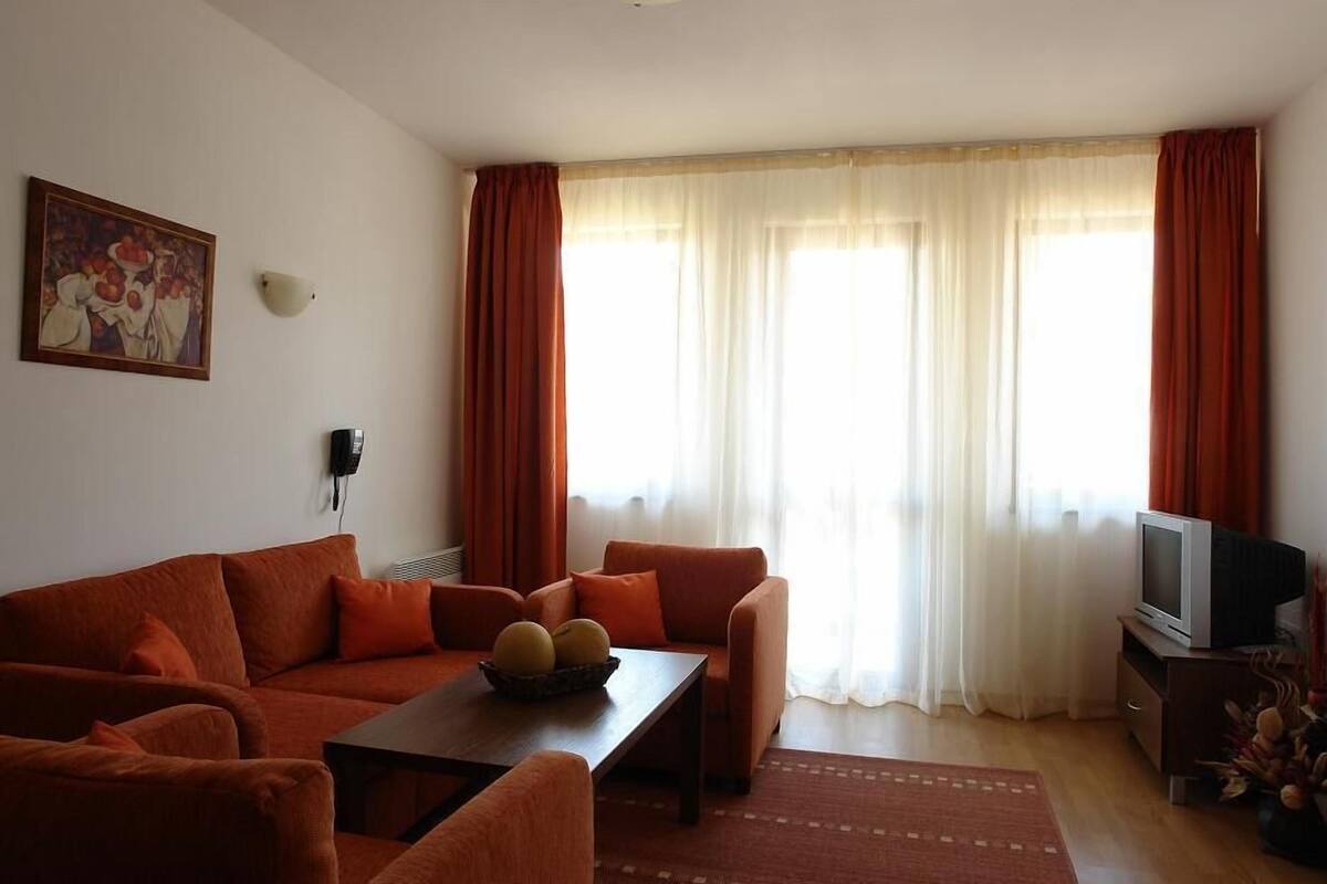 A living room with a sofa set, a coffee table with fruit, a television, and a painting on the wall.
