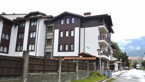 A multi-story building with balconies, a sign indicating a restaurant, and a view of mountains in the background. - Winslow Elegance Apartments (Bansko)