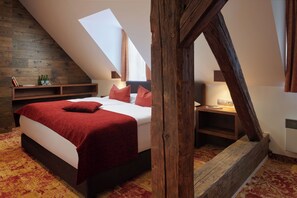 A bedroom with a sloped ceiling, a bed with red bedding, a nightstand with a lamp, and a wooden headboard.