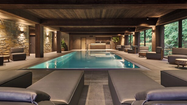Un espace piscine intérieur moderne, avec des murs en pierre, des poutres en bois et des sièges confortables.
