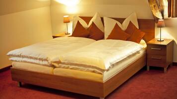 A neatly made bed with a wooden frame and a red carpeted floor. There are two bedside tables with lamps on either side of the bed.