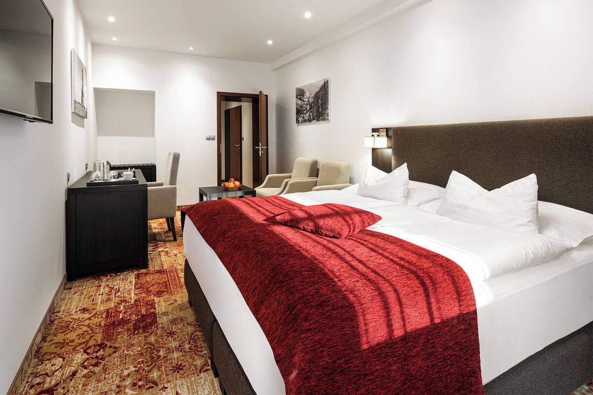 A hotel room with a large bed, a desk with a computer, a chair, and a TV on the wall.