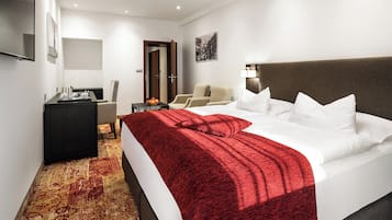 A hotel room with a large bed, a desk with a computer, a chair, and a TV on the wall.