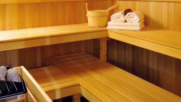 Un sauna avec des bancs en bois, un banc avec une serviette et un seau, et un banc avec un plateau de pierres.