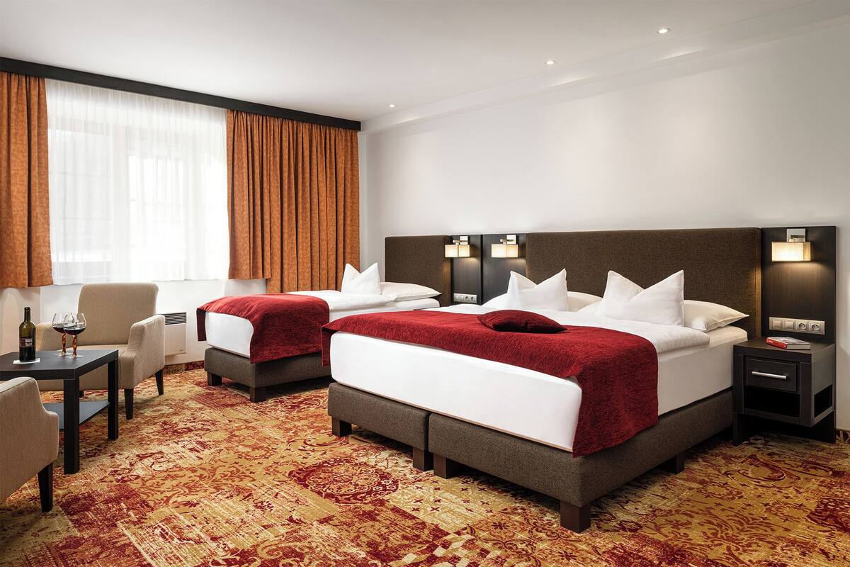 A hotel room with two beds, a sitting area with a table and chairs, and a large window with curtains.