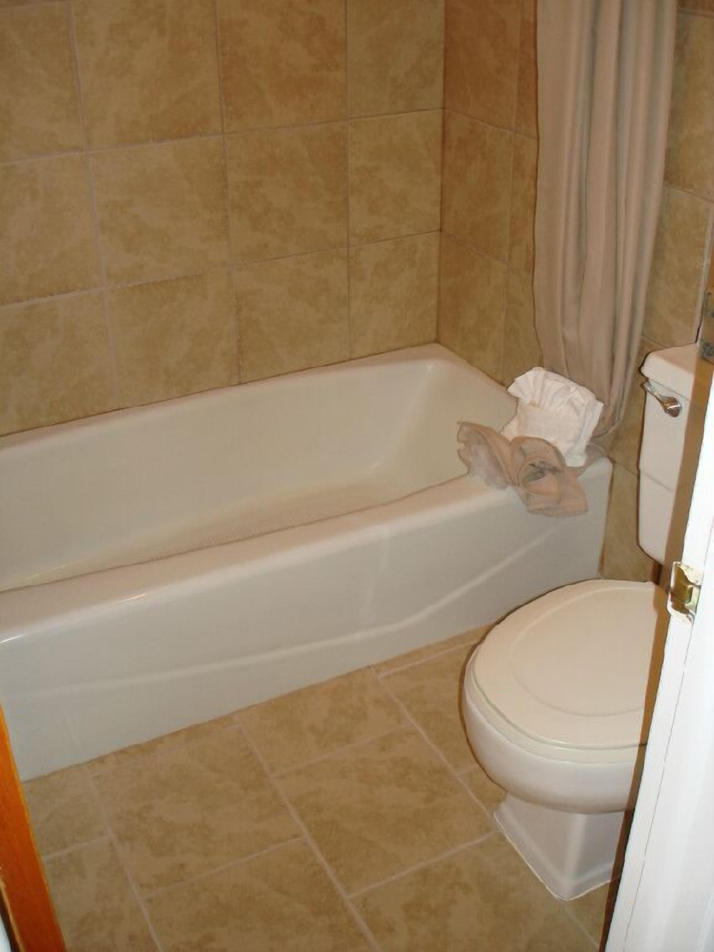 A bathroom with a bathtub, toilet, and beige tiled walls.