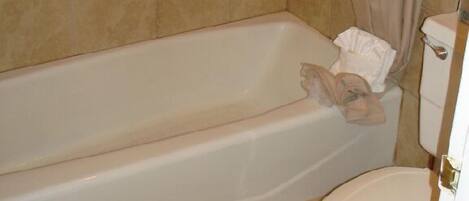 A bathroom with a bathtub, toilet, and beige tiled walls.