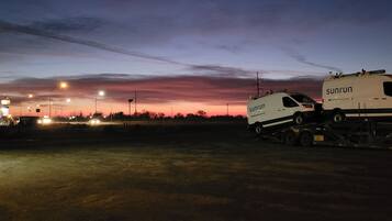 Twee busjes geparkeerd op een vlakke ondergrond, met een zonsondergang op de achtergrond.