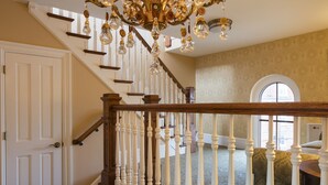 A grand staircase with white balusters and a wooden handrail, leading to a room with patterned wallpaper and a large arched window. - Washington House Hotel (Sellersville)