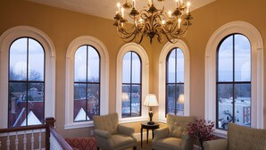 A spacious room with a grand chandelier, multiple arched windows, and a cozy seating area with patterned armchairs and a red sofa. - Washington House Hotel (Sellersville)