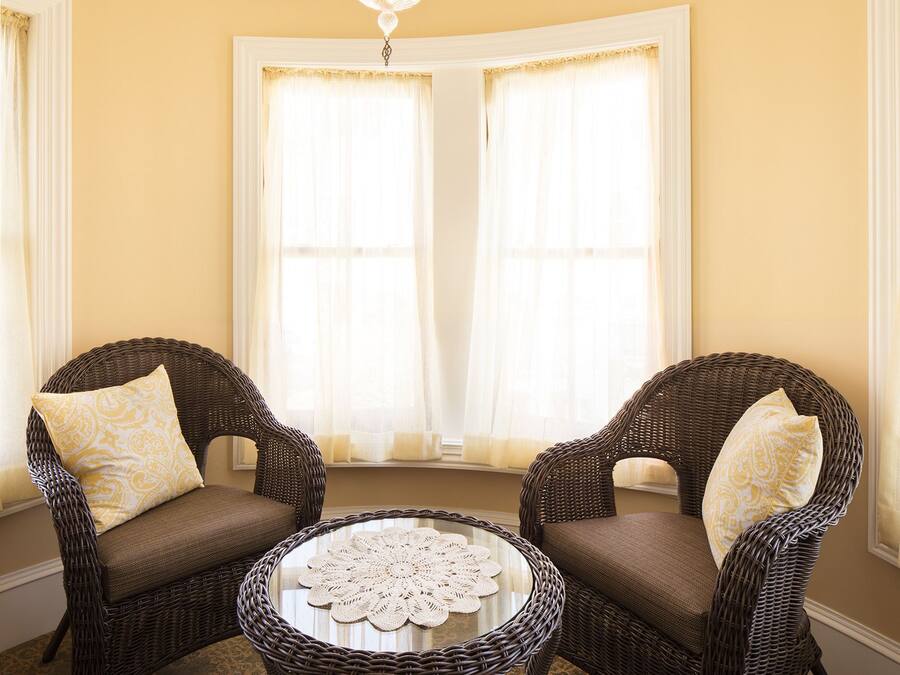 A room with two wicker chairs, a round table with a doily, and a chandelier.