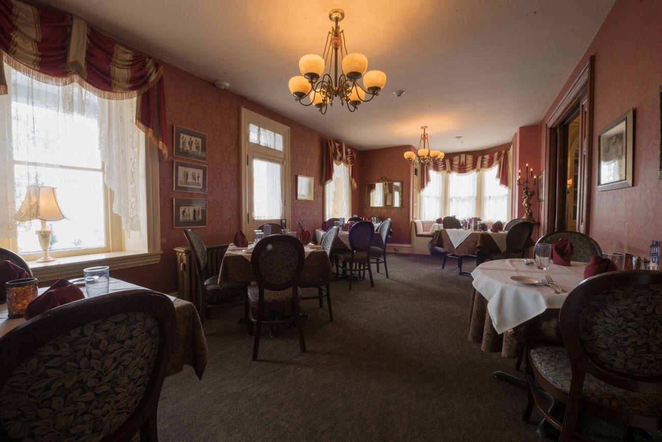 A dining area with multiple tables and chairs, chandeliers, and framed pictures on the walls.