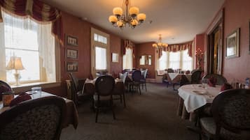 A dining area with multiple tables and chairs, chandeliers, and framed pictures on the walls.