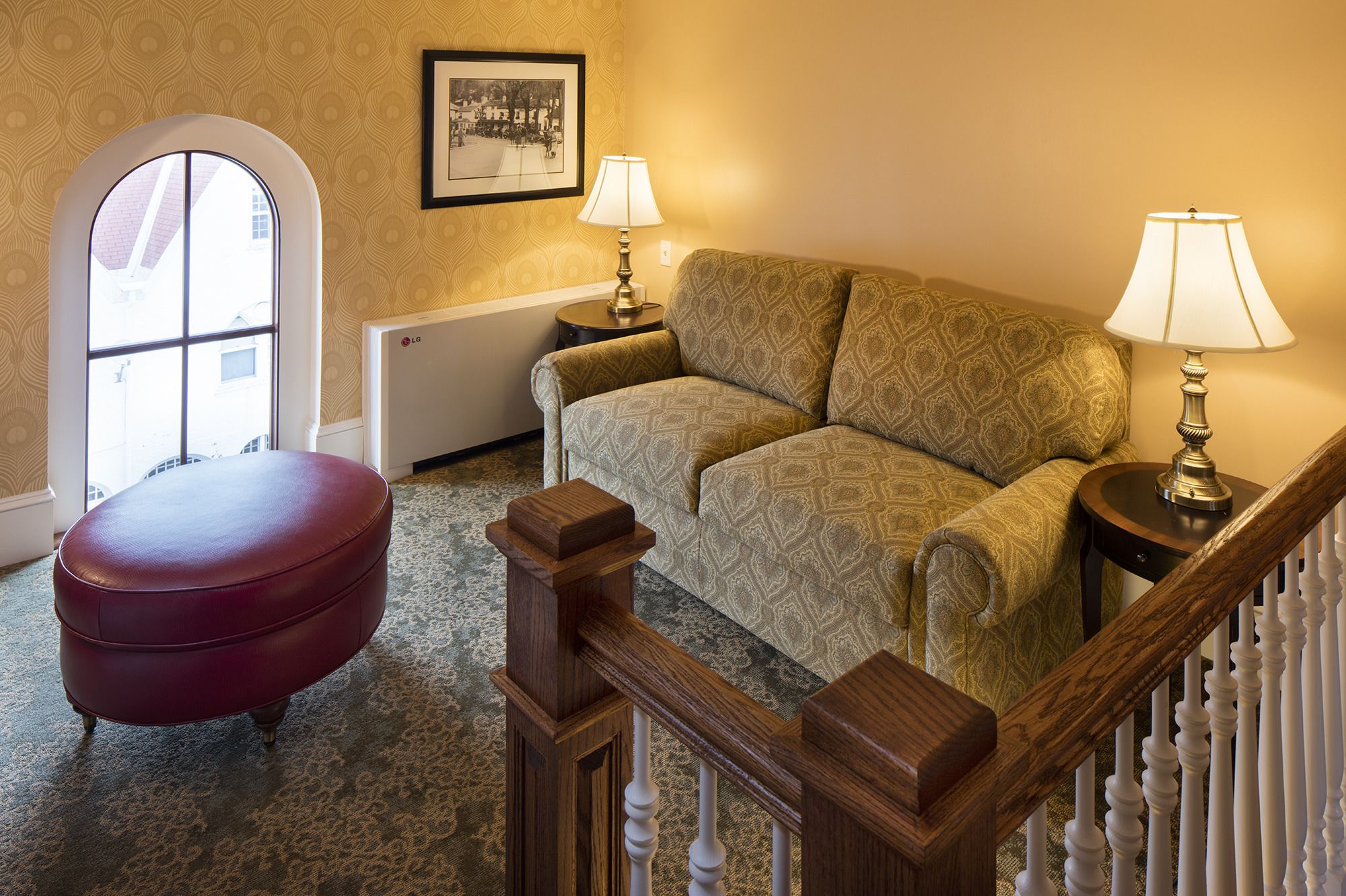 A cozy living room with a patterned sofa, a red ottoman, a framed picture on the wall, and a radiator.
