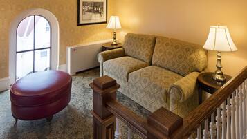 A cozy living room with a patterned sofa, a red ottoman, a framed picture on the wall, and a radiator.