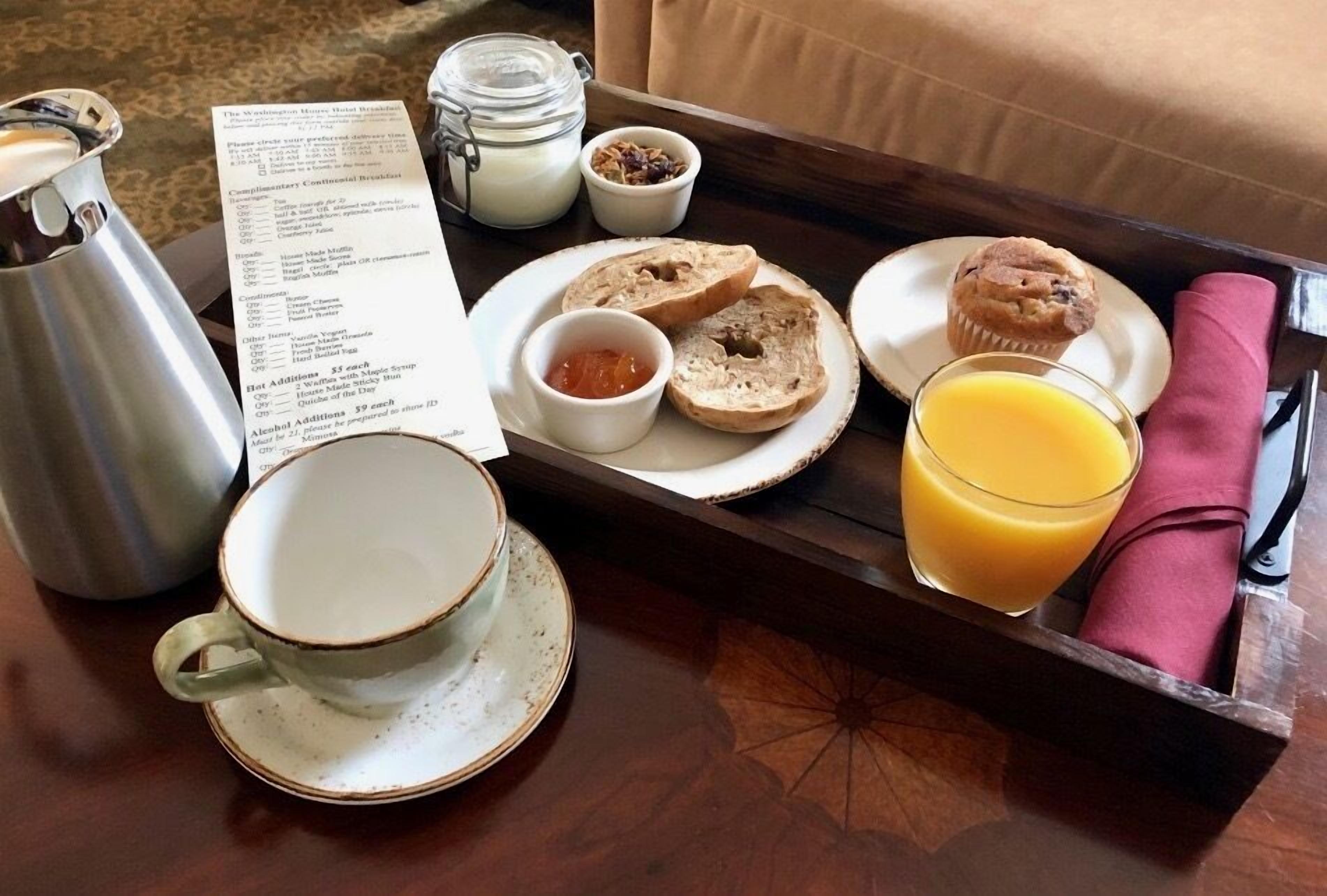 Un vassoio per la colazione con bagel, muffin, un bicchiere di succo d'arancia, una tazza, un thermos e un menu.