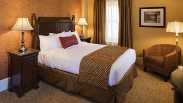 A hotel room with a large bed, two bedside tables with lamps, a chair, a framed picture on the wall, and a window with curtains.