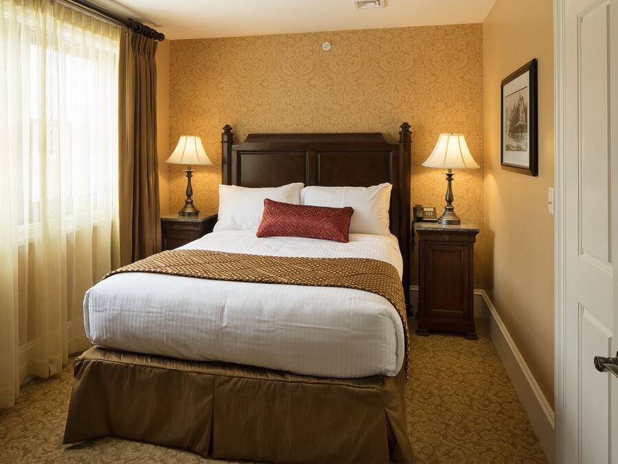 Quarto de hotel com uma cama grande, duas mesas de cabeceira com abajures, uma porta e um papel de parede estampado.