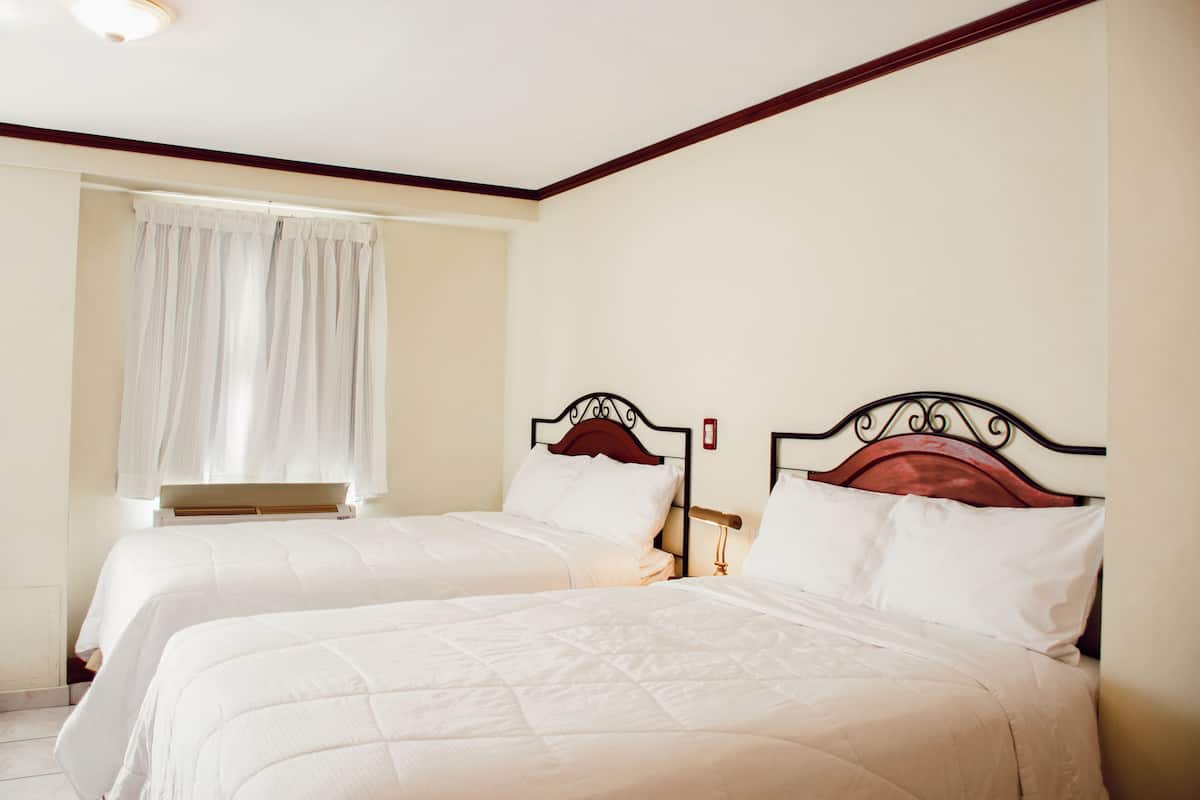 Ein Hotelzimmer mit zwei Betten, einem Fenster mit Vorhängen, einem Nachttisch mit Lampe und einer Deckenleuchte.