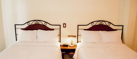 A hotel room with two single beds, a nightstand with a lamp, and a small table between the beds.