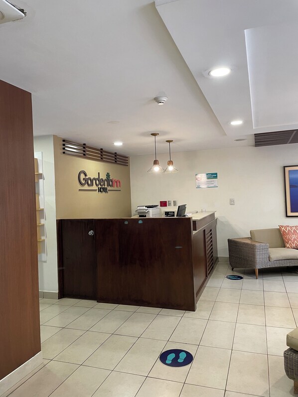 Zona de recepción de un hotel con un mostrador de madera, un cartel que dice "Gondetinn Hotel" y un área de descanso con un sofá y una silla.