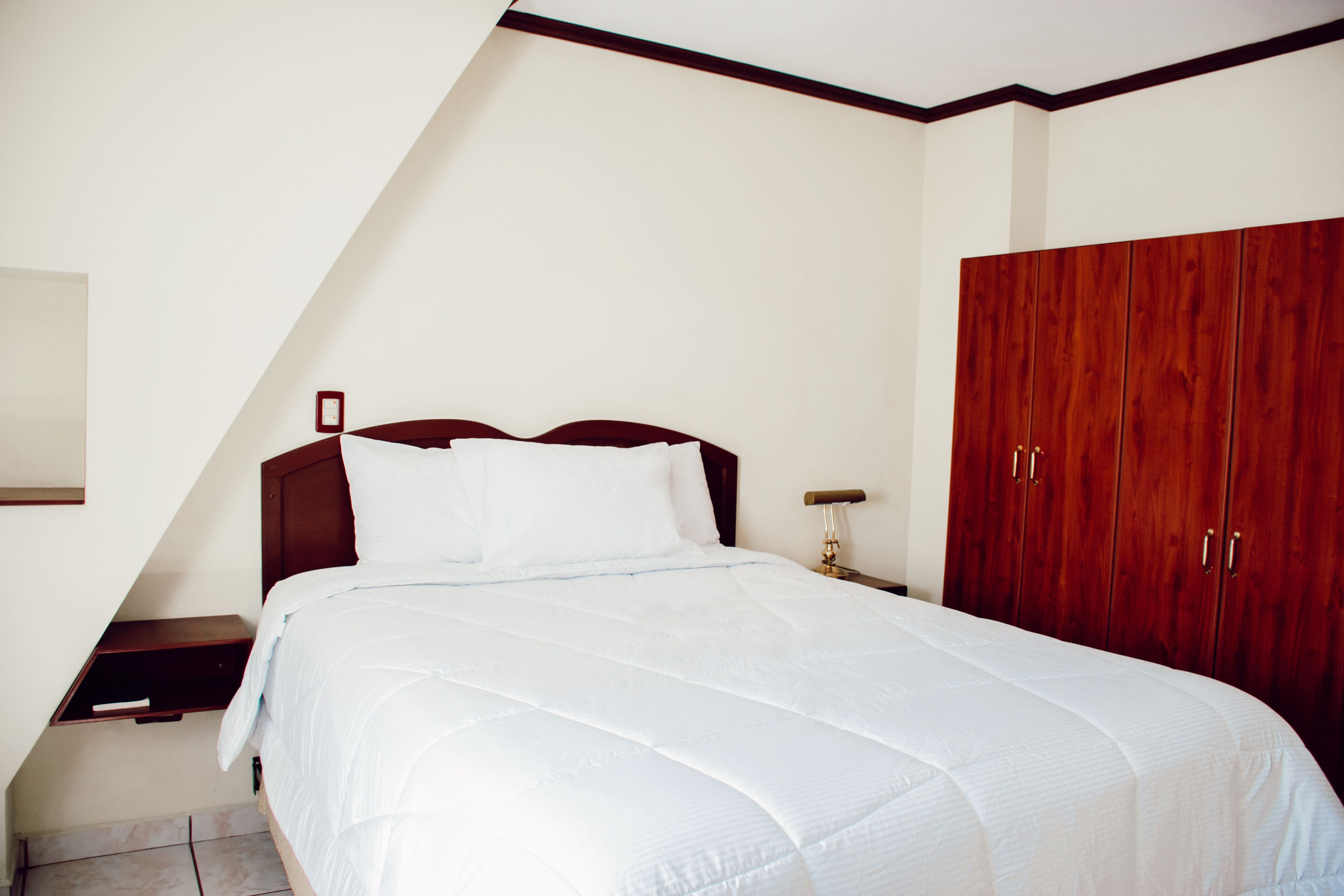 Un dormitorio con cama, mesita de noche, armario de madera y techo inclinado.