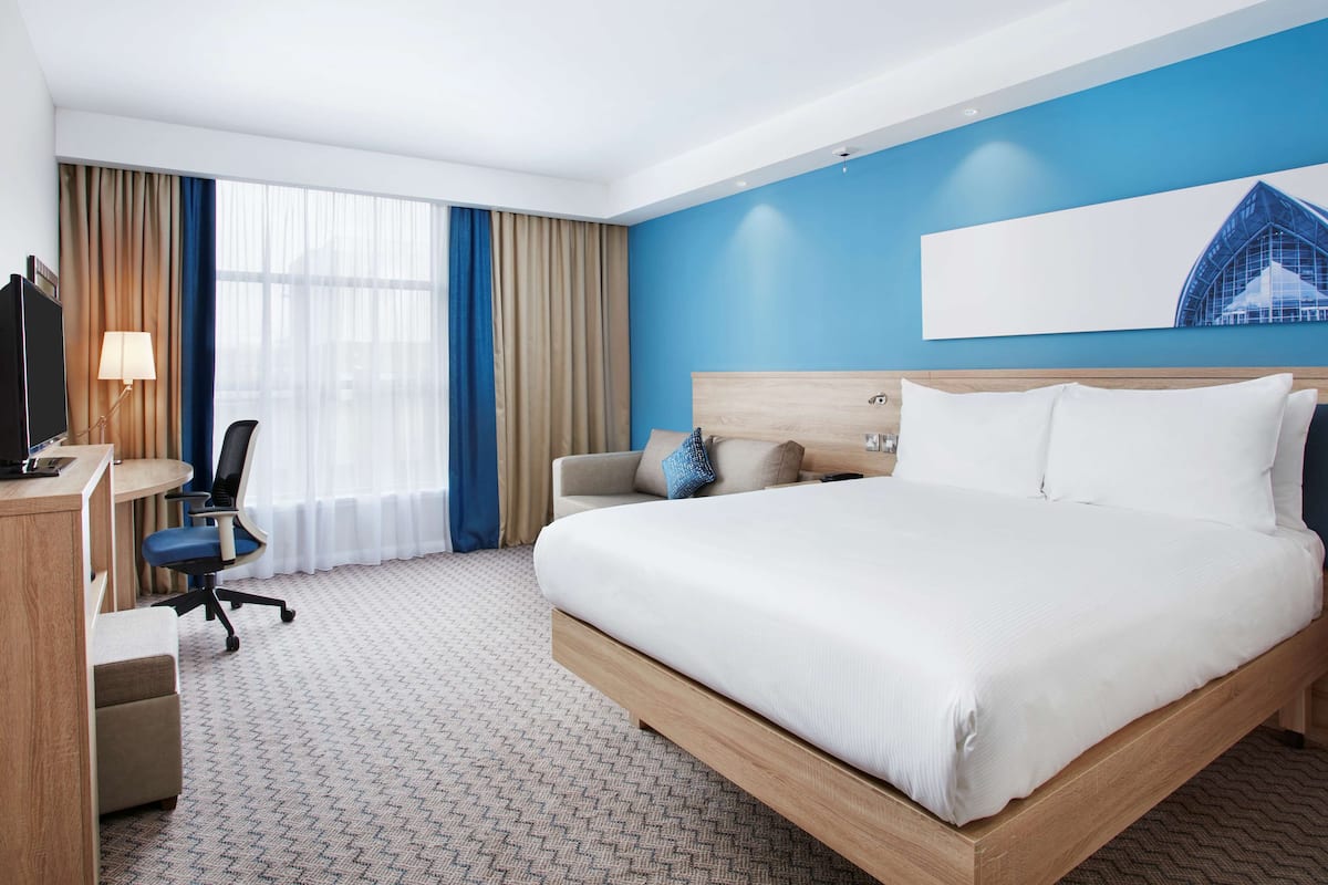 A hotel room with a large bed, a desk with a chair, a sofa, and a TV.