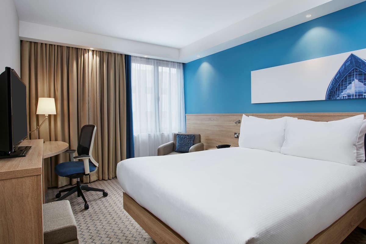 A hotel room with a large bed, a desk with a computer, a chair, and a TV.