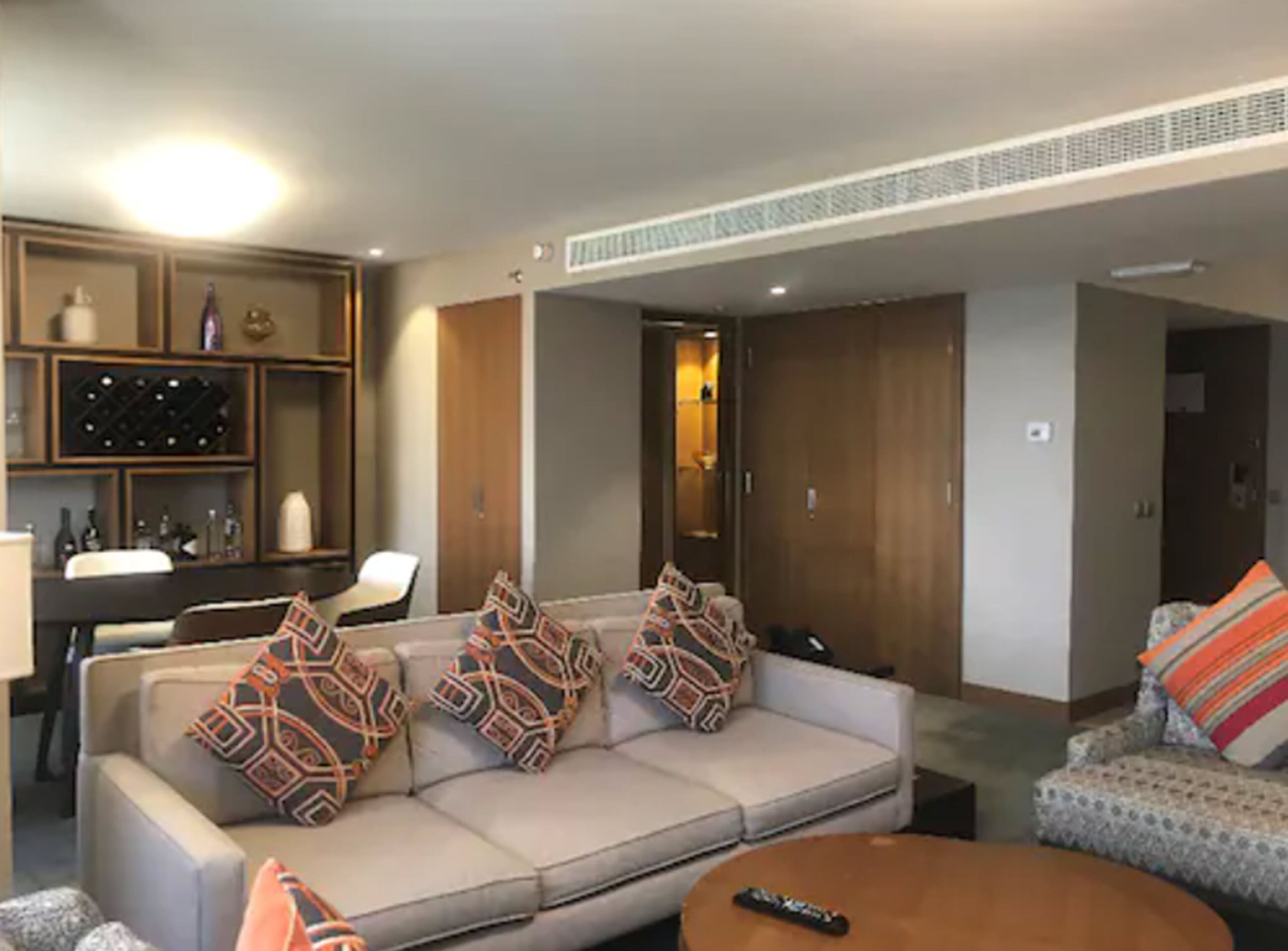 A living room with a sofa, a coffee table, and a television. There is a wine rack and a cabinet in the background.