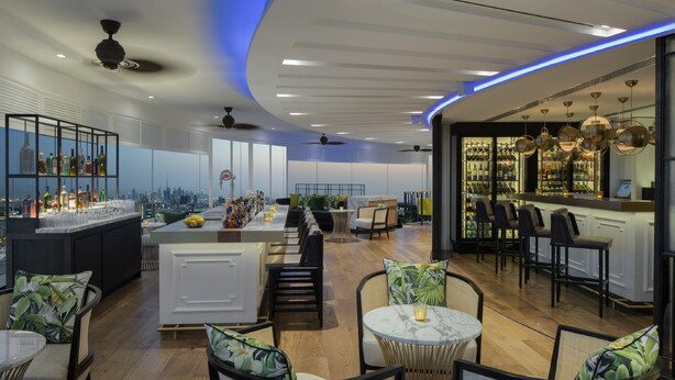 Un espace bar moderne avec vue sur la ville, des coins salons et une variété de bouteilles exposées sur des étagères.