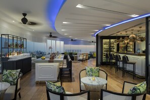 A modern bar area with a city view, seating arrangements, and a variety of bottles on shelves.