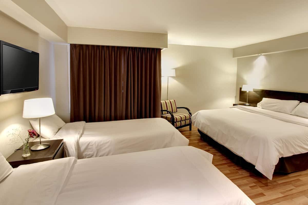 A hotel room with two beds, a TV, a chair, and a lamp.