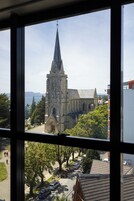 Una chiesa con un campanile slanciato e una torre dell'orologio, circondata da alberi e auto parcheggiate.